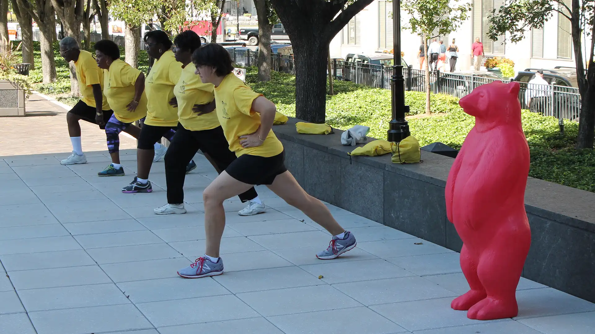 A group of people exercising next to a red bear statue.